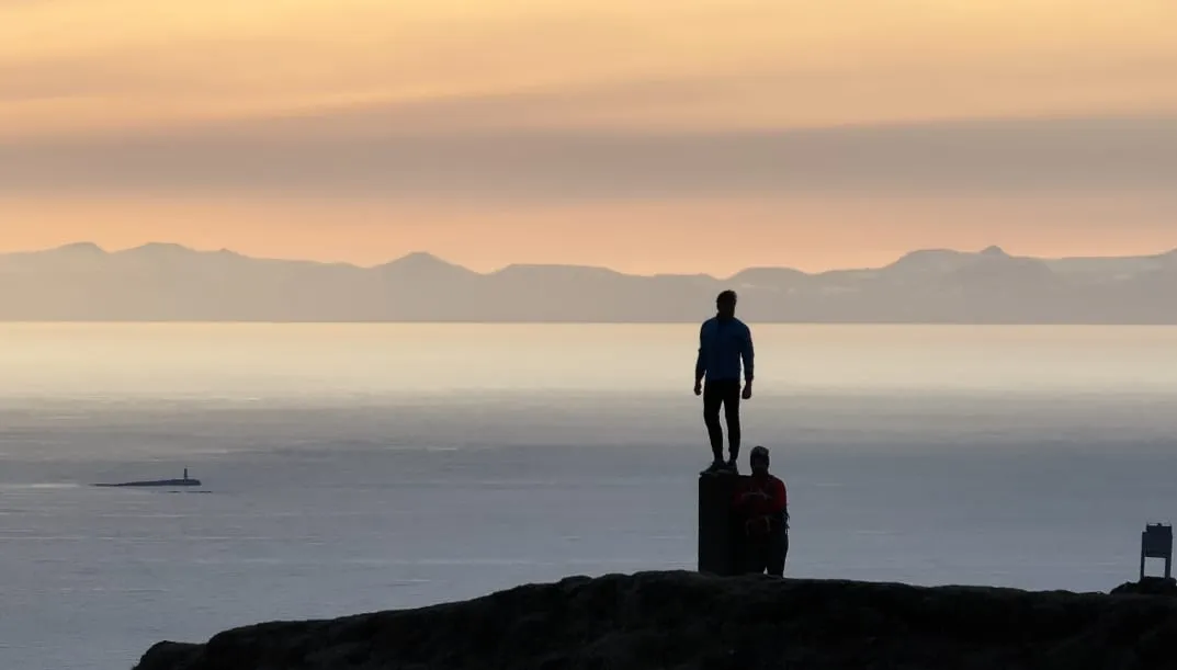 Two people at dusk on a high vantage, looking out over the sea